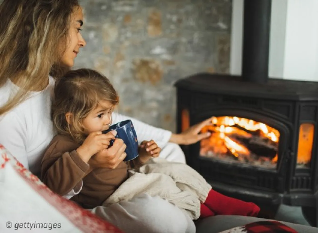 Vrouw met kind op schoot voor de kachel